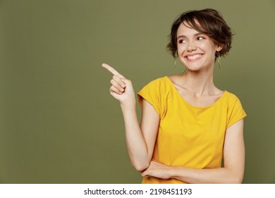 Young smiling fun woman she 20s wear yellow t-shirt indicate point index finger aside on workspace area mock up isolated on plain olive green khaki background studio portrait. People lifestyle concept