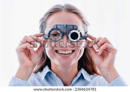 Young smiling girl is fitting special ophthalmic glasses to check up her vision isolated over white background. Eyesight health checkup. Selecting lenses spectacles