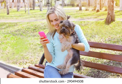 Young Smiling Girl Owner Holding Phone With Yorkshire Terrier Dog Sitting In Park