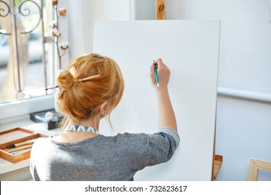Young smiling girl paints on canvas with oil colors in own workshop. Window on the background. Art concept. - Shutterstock ID 732623617