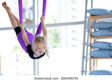  young smiling girl practice in aero stretching swing in purple hammock in fitness club. kids Aerial flying yoga exercises. - Powered by Shutterstock