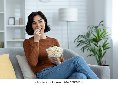 Young smiling girl resting at home. Sitting on the sofa, holding a bowl of popcorn and eating snacks. - Powered by Shutterstock