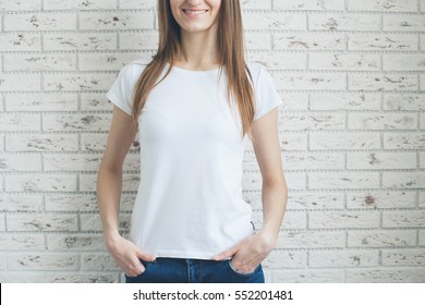 Young smiling girl wearing blank t-shirt. Brick white wall in the background.