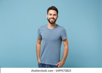 Young smiling handsome man in casual clothes posing isolated on blue wall background, studio portrait. People sincere emotions lifestyle concept. Mock up copy space. Holding hands in pockets
