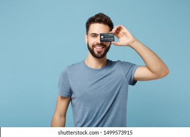 Young smiling handsome man in casual clothes posing isolated on blue wall background studio portrait. People sincere emotions lifestyle concept. Mock up copy space. Covering eye with credit bank card