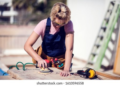 Young Smiling Handy Woman With Short Blond Hair Sanding Wooden Surface. 