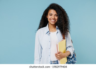 Young Smiling Happy African American Girl Teen Student Wear Denim Clothes Backpack Hold Books Isolated On Blue Color Background Studio Portrait. Education In High School University College Concept.