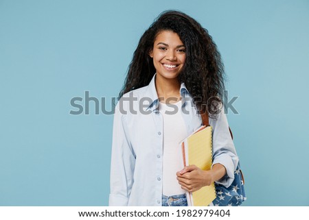Young smiling happy african american girl teen student wear denim clothes backpack hold books isolated on blue color background studio portrait. Education in high school university college concept.