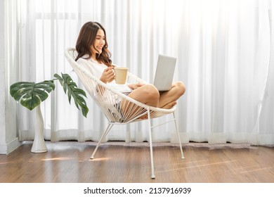 Young Smiling Happy Beautiful Asian Woman Relaxing Using Laptop Computer In The Bedroom At Home.Young Creative Girl Working And Typing On Keyboard.work From Home Concept