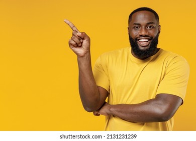 Young smiling happy black man 20s wearing bright casual t-shirt point index finger aside on workspace area mock up isolated on plain yellow color background studio portrait. People lifestyle concept