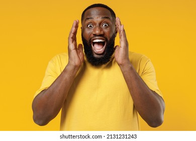 Young Smiling Happy Black Man 20s Wearing Bright Casual T-shirt Scream Hot News About Sales Discount With Hands Near Mouth Isolated On Plain Yellow Color Background Studio. People Lifestyle Concept