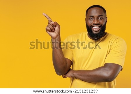 Young smiling happy black man 20s wearing bright casual t-shirt point index finger aside on workspace area mock up isolated on plain yellow color background studio portrait. People lifestyle concept
