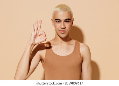 Young Smiling Happy Blond Latin American Hispanic Gay Man 20s With Make Up In Beige Tank Shirt Show Okay Gesture Isolated On Plain Light Ocher Background Studio Portrait People Lgbt Lifestyle Concept.