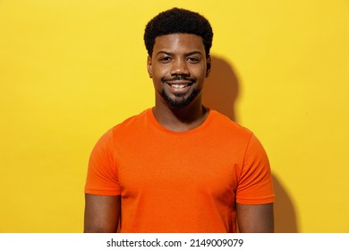 Young Smiling Happy Calm Unshaven Man Of African American Ethnicity 20s In Basic Casual Orange T-shirt Look Camera Isolated On Plain Yellow Color Background Studio Portrait. People Lifestyle Concept