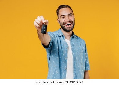 Young smiling happy caucasian man 20s wearing blue shirt white t-shirt hold give car key fob keyless system look camera isolated on plain yellow background studio portrait. People lifestyle concept