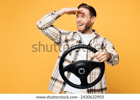 Young smiling happy Caucasian man wear brown shirt casual clothes hold steering wheel driving car look far away distance isolated on plain yellow orange background studio portrait. Lifestyle concept