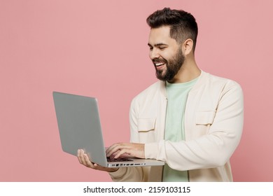 Young Smiling Happy Cheerful Caucasian Man 20s Wearing Trendy Jacket Shirt Hold Use Work On Laptop Pc Computer Isolated On Plain Pastel Light Pink Background Studio Portrait. People Lifestyle Concept