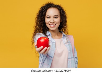 Young Smiling Happy Cheerful Cool Black Teen Girl Student She Wearing Casual Clothes Backpack Bag Hold Giving Apple Isolated On Plain Yellow Color Background. High School University College Concept