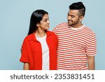 Young smiling happy cheerful couple two friends family Indian man woman wear red casual clothes t-shirts together look to each other isolated on pastel plain light blue cyan color background studio
