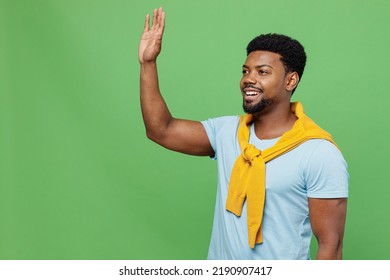 Young Smiling Happy Cheerful Friendly Fun Man Of African American Ethnicity 20s Wear Blue T-shirt Waving Hand Say Hello Hi Isolated On Plain Green Background Studio Portrait. People Lifestyle Concept