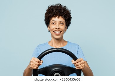 Young smiling happy cheerful fun woman of African American ethnicity wear t-shirt casual clothes hold steering wheel driving car isolated on plain pastel light blue cyan background. Lifestyle concept - Powered by Shutterstock