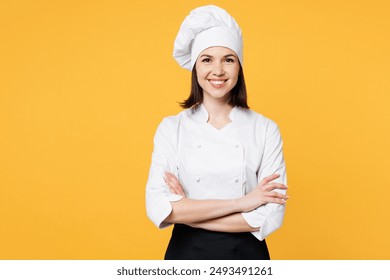 Young smiling happy chef cook baker woman wear white shirt black apron uniform toque chefs hat hold hands crossed folded look camera isolated on plain yellow background studio. Cooking food concept - Powered by Shutterstock