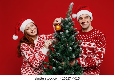 Young smiling happy couple friends two man woman 20s in sweater hat hold fir-tree decorating isolated on plain red background studio. Happy New Year 2022 celebration merry ho x-mas holiday concept. - Powered by Shutterstock