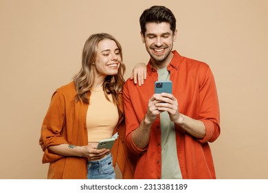 Young smiling happy couple two friends family man woman wear casual clothes hold in hand use mobile cell phone together chatting isolated on pastel plain light beige color background studio portrait - Shutterstock ID 2313381189