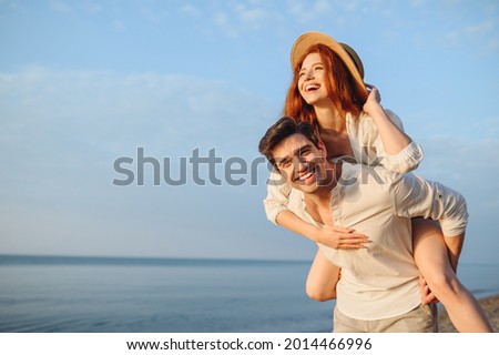 Young smiling happy couple two friends family man woman in white clothes boyfriend give piggyback ride to joyful, girlfriend sit on back at sunrise over sea beach ocean outdoor seaside in summer day