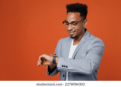 Young smiling happy employee business man corporate lawyer wear classic formal grey suit shirt glasses work in office use look at smart watch check time isolated on plain red orange background studio - Powered by Shutterstock