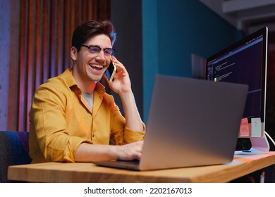 Young Smiling Happy Employee Businessman Lawyer Software Engineer IT Specialist Programmer Man 20s Wearing Shirt Work At Office On Laptop Pc Computer Talk Speak On Mobile Cell Phone Occupation Concept