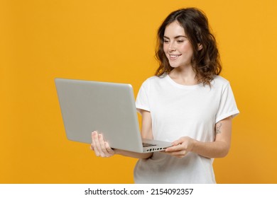 Young smiling happy freelancer copywriter caucasian student woman in white basic t-shirt look camera hold laptop pc computer chat browsing isolated on yellow orange color background studio portrait - Powered by Shutterstock