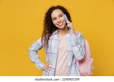 Young Smiling Happy Fun Black Teen Girl Student She Wear Casual Clothes Backpack Bag Talk Speak On Mobile Cell Phone Isolated On Plain Yellow Color Background. High School University College Concept