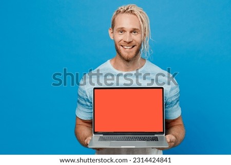 Young smiling happy fun blond man with dreadlocks 20s he wear white t-shirt hold use work on laptop pc computer with blank screen workspace area isolated on plain pastel light blue background studio.