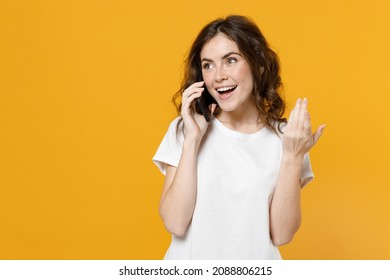 Young smiling happy fun caucasian woman in white basic casual t-shirt talking speak on mobile phone conducting pleasant conversation spread hand solated on yellow orange background studio portrait