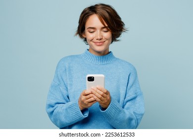 Young smiling happy fun caucasian woman wear knitted sweater hold in hand use mobile cell phone chatting isolated on plain pastel light blue cyan background studio portrait. People lifestyle concept - Powered by Shutterstock