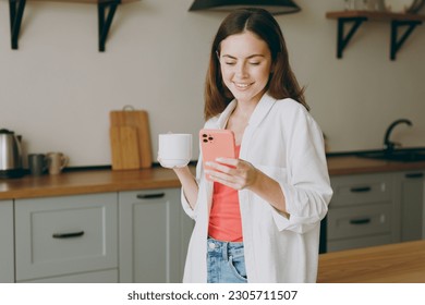 Young smiling happy fun cheerful housewife woman wearing casual clothes drink coffee use mobile cell phone chat online eat breakfast cooking food in light kitchen at home alone. Healthy diet concept - Powered by Shutterstock