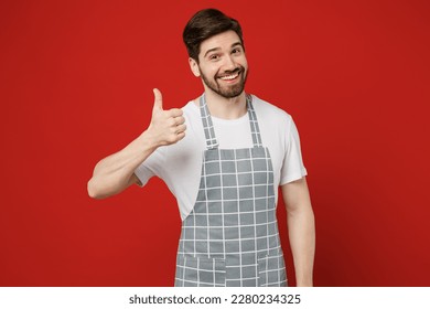 Young smiling happy fun cool satisfied male housewife housekeeper chef cook baker man in grey apron showing thumb up like gesture isolated on plain red color background studio. Cooking food concept - Powered by Shutterstock