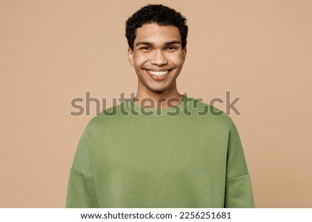 Young smiling happy fun cool cheerful man of African American ethnicity wearing green sweatshirt look camera isolated on plain pastel light beige background studio portrait. People lifestyle concept