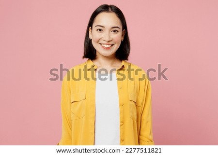 Young smiling happy fun cool cheerful student woman of Asian ethnicity wear yellow shirt white t-shirt looking camera isolated on plain pastel light pink background studio portrait. Lifestyle concept