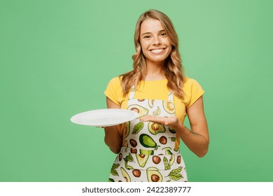 Young smiling happy fun housewife housekeeper chef cook baker woman wear apron yellow t-shirt hold in hand point on empty plate isolated on plain pastel green background studio. Cooking food concept - Powered by Shutterstock