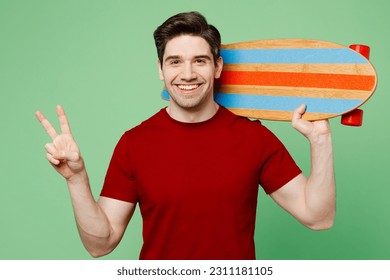 Young smiling happy fun man he wears red t-shirt casual clothes hold skateboard pennyboard behind neck show v-sign isolated on plain pastel light green background studio portrait. Lifestyle concept - Powered by Shutterstock
