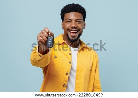 Young smiling happy fun man of African American ethnicity 20s wear yellow shirt hold giving car keys fob keyless system isolated on plain pastel light blue background studio. People lifestyle concept