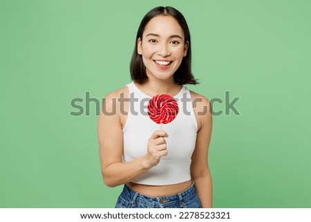 Young smiling happy fun positive woman wear white clothes hold round lollipop look camera isolated on plain pastel light green background. Proper nutrition healthy fast food unhealthy choice concept