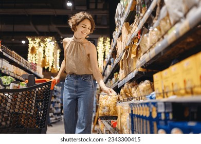 Young smiling happy fun satisfied woman 20s wearing casual clothes shopping at supermaket store buy choosing pasta go with grocery cart inside hypermarket. People purchasing gastronomy food concept. - Powered by Shutterstock