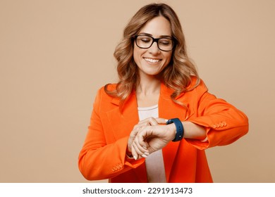 Young smiling happy fun successful employee business woman corporate lawyer 30s wear classic formal orange suit glasses smart watch check time work in office isolated on plain beige background studio