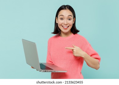 Young Smiling Happy Fun Woman Of Asian Ethnicity 20s Wearing Pink Sweater Hold Use Work Point Index Finger On Laptop Pc Computer Isolated On Pastel Plain Light Blue Color Background Studio Portrait.