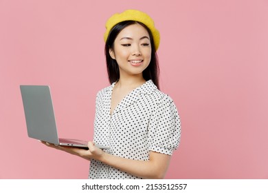 Young Smiling Happy Fun Woman Of Asian Ethnicity 20s In White Polka Dot T-shirt Yellow Beret Hold Use Work On Laptop Pc Computer Look Aside On Workspace Area Isolated On Plain Pastel Pink Background.