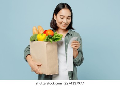 Young smiling happy fun woman wear casual clothes hold brown paper bag with food products look at check isolated on plain blue cyan background studio portrait. Delivery service from shop or restaurant