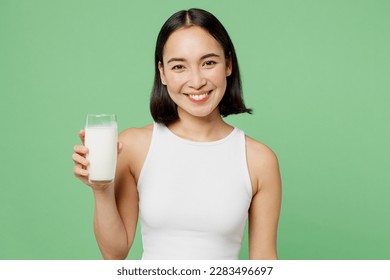 Young smiling happy fun woman wear white clothes hold in hand glass drink milk look camera isolated on plain pastel light green background. Proper nutrition healthy fast food unhealthy choice concept